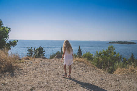 adorable child with long blond hair in blue dress having romantic time in historic streets back viewの写真素材