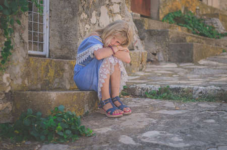 adorable child with long blond hair in blue dress having romantic time in historic streets back viewの写真素材