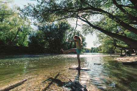 cute girl with long hair back view standing in the river shore relaxing in green scenic nature in sunny golden hour day timeの写真素材