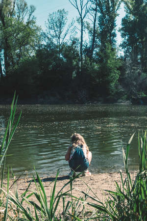 cute girl with long hair back view standing in the river shore relaxing in green scenic nature in...