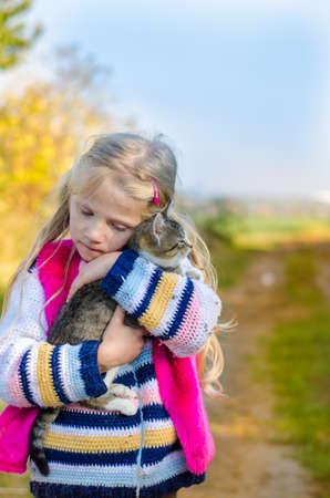 little child holding domestic cat and walking alone in sunny autumnal atmosphereの写真素材