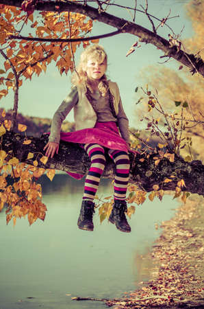 little child sitting in in the tree branch over the blue lake in scenic sunset time in colorful countrysideの写真素材