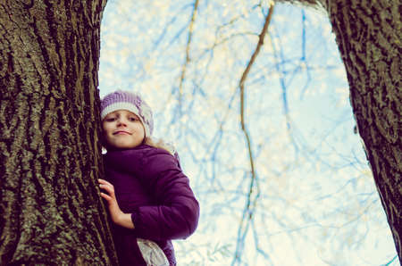 little child sitting in in the tree branch over the blue lake in scenic sunset time in colorful countrysideの写真素材