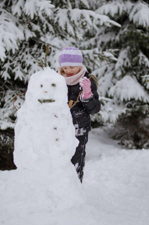 two beautiful girl having fun with snowman in winter forestの写真素材