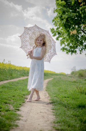 adorable blond child in rural path having fun with white lace umbrellaの写真素材