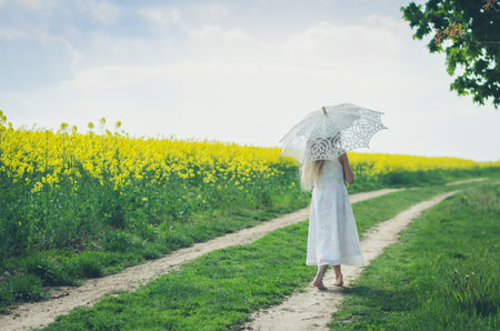 adorable blond child in rural path having fun with white lace umbrellaの写真素材