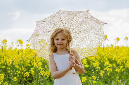 adorable blond child in rural path having fun with white lace umbrellaの写真素材