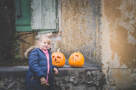 lvoely girl two orange carved halloween pumpkins in front of the houseの写真素材