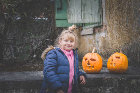 lovely girl two orange carved halloween pumpkins in front of the houseの写真素材