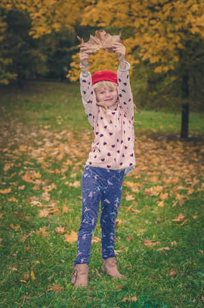 adorable blond girl in colorful jacket enjoying color of autumnal leavesの写真素材
