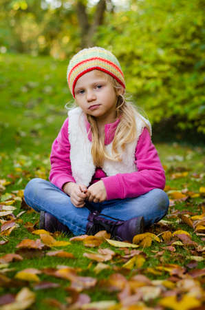 portrait of happy smiling girl with long blond hair in colorful autumnal atmosphere posing in green park full of fallen leavesの写真素材