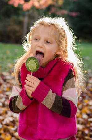 portrait of happy smiling girl with long blond hair in colorful autumnal atmosphere posing in green park full of fallen leavesの写真素材