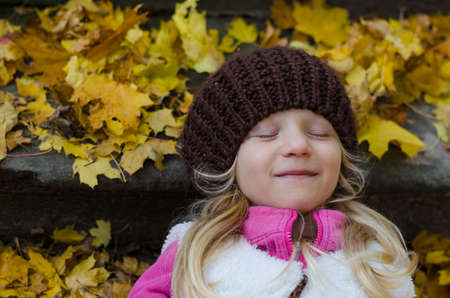 portrait of happy smiling girl with long blond hair in colorful autumnal atmosphere posing in green park full of fallen leavesの写真素材