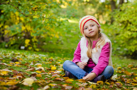 portrait of happy smiling girl with long blond hair in colorful autumnal atmosphere posing in green park full of fallen leavesの写真素材