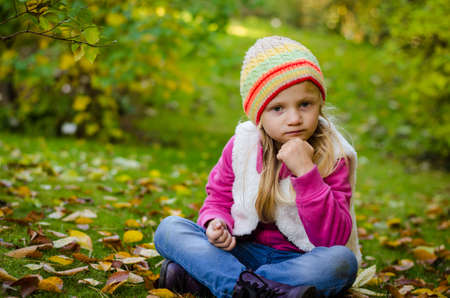 portrait of happy smiling girl with long blond hair in colorful autumnal atmosphere posing in green park full of fallen leavesの写真素材