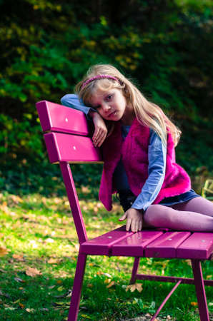portrait of happy smiling girl with long blond hair in colorful autumnal atmosphere posing in green park full of fallen leavesの写真素材