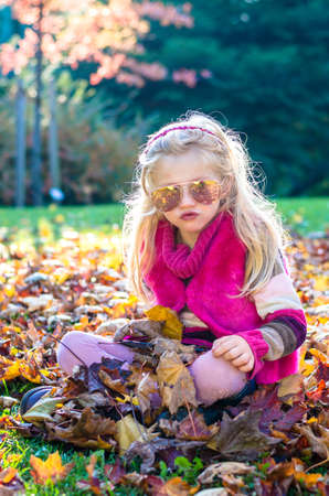 portrait of happy smiling girl with long blond hair in colorful autumnal atmosphere posing in green park full of fallen leavesの写真素材