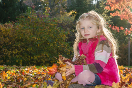 portrait of happy smiling girl with long blond hair in colorful autumnal atmosphere posing in green park full of fallen leavesの写真素材