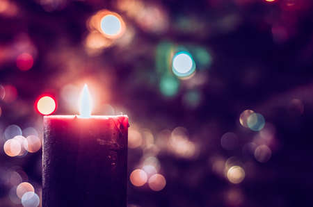 one burning candle concept with shining bokeh glittering ligts on christmas tree on dark background