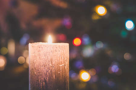 one burning candle concept with shining bokeh glittering ligts on christmas tree on dark background