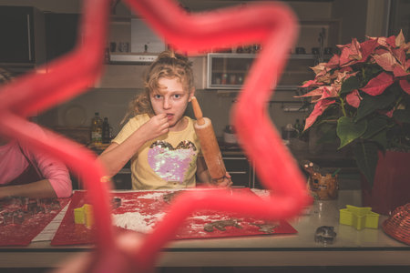 lovely child girl tasting and enjoying sweet color paste while cooking gingerbread cookies for christmas tableの写真素材