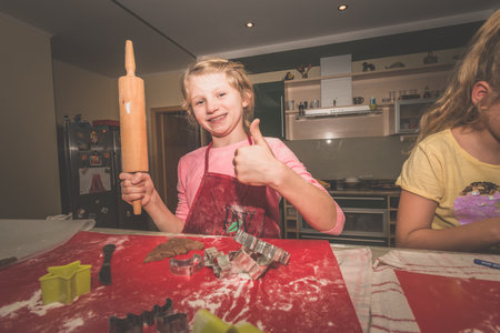 lovely child girl tasting and enjoying sweet color paste while cooking gingerbread cookies for christmas tableの写真素材