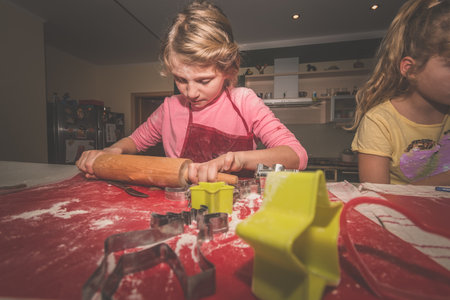lovely child girl tasting and enjoying sweet color paste while cooking gingerbread cookies for christmas tableの写真素材
