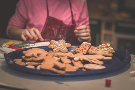lovely child girl tasting and enjoying sweet color paste while cooking gingerbread cookies for...