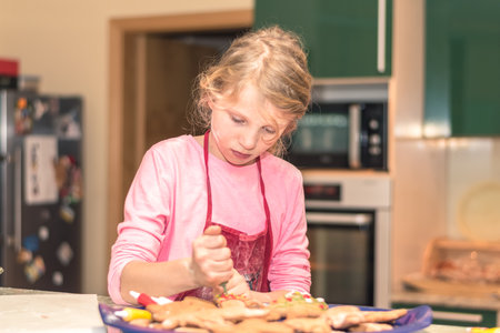 lovely child girl tasting and enjoying sweet color paste while cooking gingerbread cookies for christmas tableの写真素材