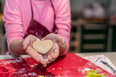 lovely child girl tasting and enjoying sweet color paste while cooking gingerbread cookies for...