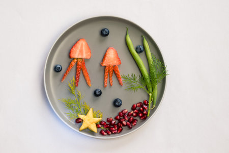 jellyfish, green plants and starfish in sea world from strawberries, blackberries, beans and pomegranate, isolated colorful food ideas on plateの写真素材