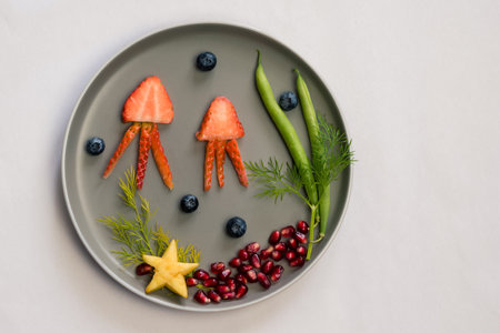 jellyfish, green plants and starfish in sea world from strawberries, blackberries, beans and pomegranate, isolated colorful food ideas on plateの写真素材
