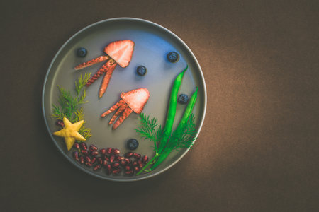 jellyfish, green plants and starfish in sea world from strawberries, blackberries, beans and pomegranate, isolated colorful food ideas on plate with brown backgroundの写真素材