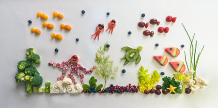 octopus, fishes, jellyfish, starfish made from red fruits, tomato, kiwi, strawberry in sea world from cauliflower, broccoli and green herbs isolated on white backgroundの写真素材