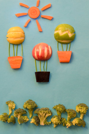 flying balloon made from apples,broccoli and carrots, isolated colorful food ideas on blue backgroundsの写真素材