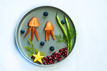 jellyfish, green plants and starfish in sea world from strawberries, blackberries, beans and pomegranate, isolated colorful food ideas on plateの写真素材