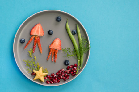 jellyfish, green plants and starfish in sea world from strawberries, blackberries, beans and pomegranate, isolated colorful food ideas on plateの写真素材
