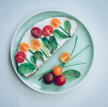 bread with butter, red and orange cherry tomatoes designed as flowers with green chives and basil herbsの写真素材