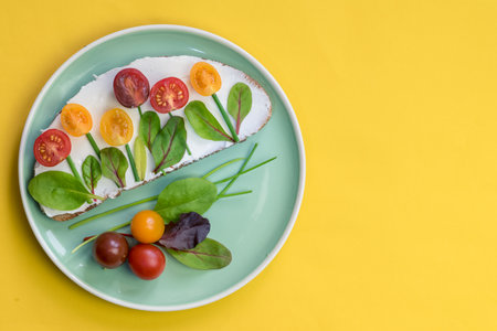 bread with butter, red and orange cherry tomatoes designed as flowers with green chives and basil herbsの写真素材