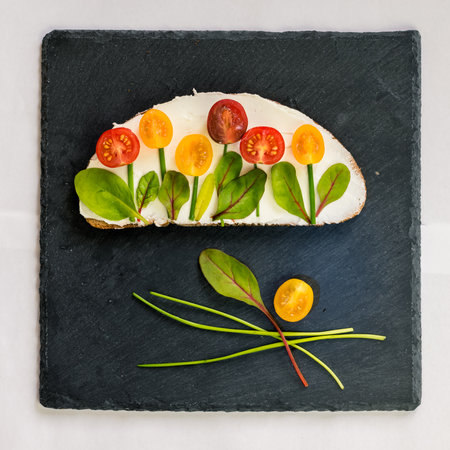 bread with butter, red and orange cherry tomatoes designed as flowers with green chives and basil herbsの写真素材