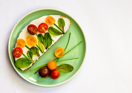 bread with butter, red and orange cherry tomatoes designed as flowers with green chives and basil herbsの写真素材