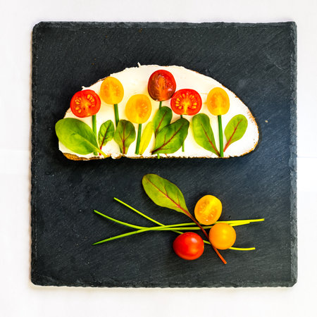bread with butter, red and orange cherry tomatoes designed as flowers with green chives and basil herbsの写真素材