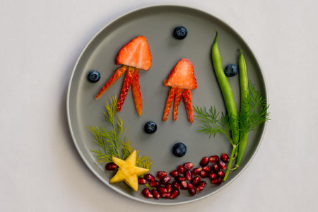 jellyfish, green plants and starfish in sea world from strawberries, blackberries, beans and pomegranate, isolated colorful food ideas on plateの写真素材