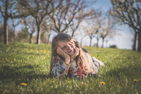 adorable girl with long blond hair lying on grass in spring park outdoorsの写真素材