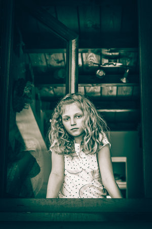 adorable girl with long blond hair looking through windowの写真素材