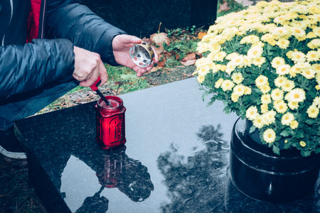 hands of man lighting candles on graves decorated with lanterns, burning candles, colorful chrysanthemum flowers, catholic symbolsの写真素材