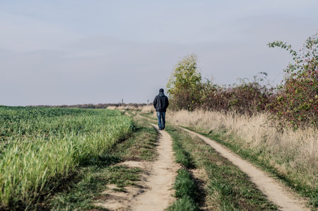 nostalgic autumn day with sad man leaving away among empty meadows in dramatic countryside