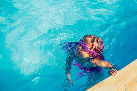 A girl in swimming glasses has fun and splashes in the pool.の写真素材