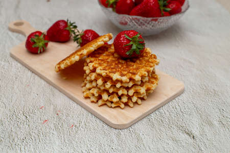 Waffles served with strawberries on a white cutting board on a gray table and a basket with ripe strawberriesの写真素材