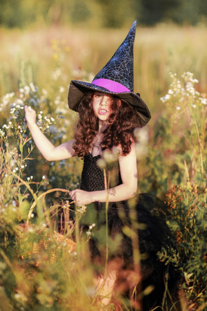 A girl in a black dress and a witchs hat collects herbs for a potion.